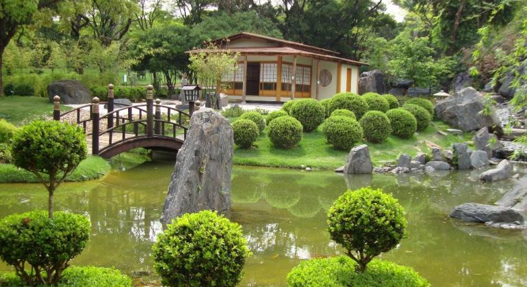 Casa, lago, ponte, árvores e pedras em Jardim Japonês