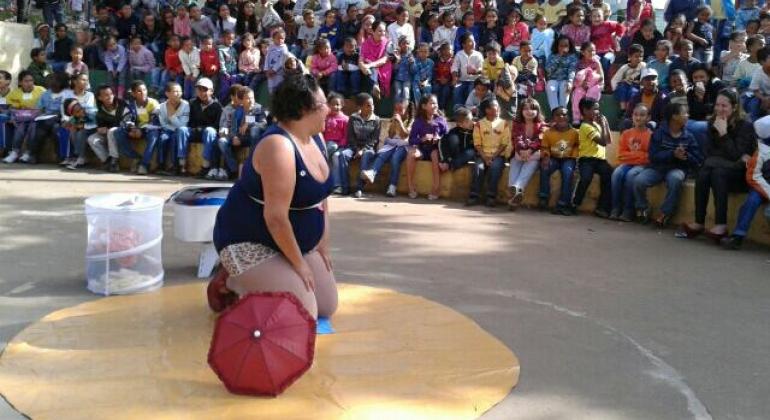 Apresentações teatrais promovidas pela Prefeitura vão incentivar visitantes de parques a refletir sobre conservação do meio ambiente. Foto: DivulgaçãoFoto: Divulgação Mulher, vestida de palanha, se apresenta para mais de 50 pessoas sentadas em escadaria circular.