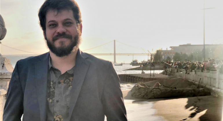 Troca de cartas entre escritores brasileiros inspiram espetáculo no Teatro Raul Belém Machado. Foto: Fernando Chagas Homem de blazer sorri; no fundo, uma praia e uma ponte, durante o dia.