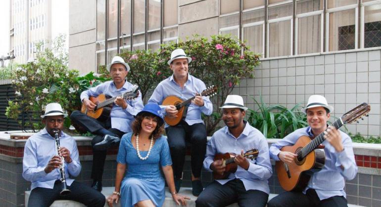 Cantora, acompanhada de cinco músicos, todos de azul, durante o dia. 