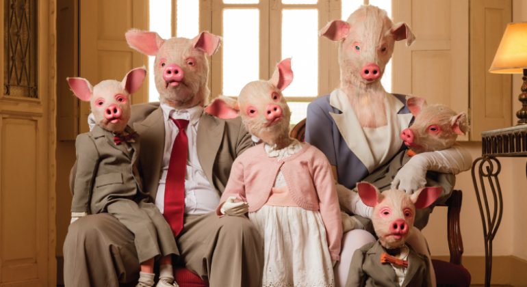 Família composta por pai, mãe e quatro filho, com máscaras de porco, sentados em ma cadeira