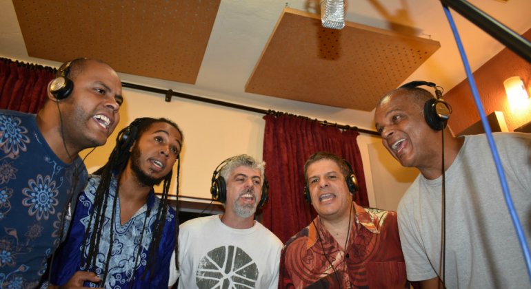 Cinco homens, em estúdio, cantando.