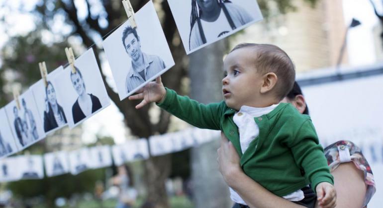 Como parte das ações da PBH para valorizar a região, Lagoinha recebe projeto que inclui exposição fotográfica e produção audiovisual. Foto: Marcus Desimoni/Nitro Mulher com criança no colo que toca fotos P&B penduradas no varal, durante o dia.