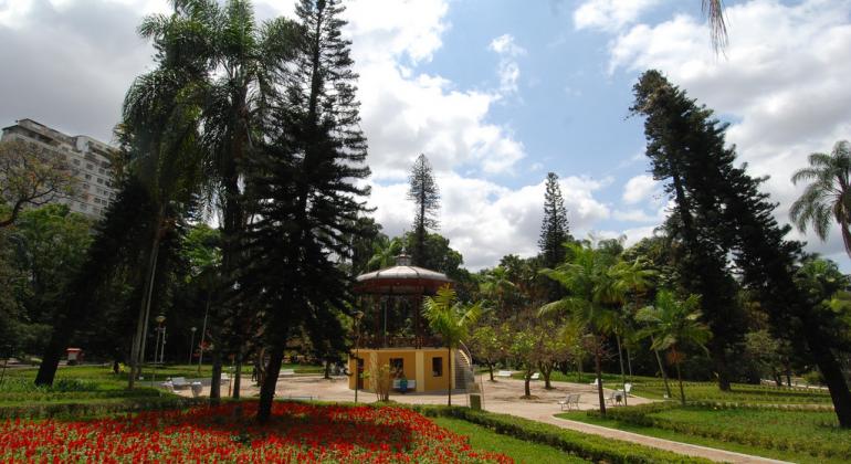 Coreto do Parque Municipal Américo Renneé Giannetti, cencado de árvores e vegetação, com prédio ao fundo, durante o dia. 
