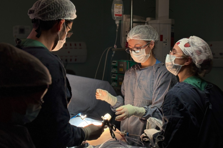 A foto mostra equipe médica composta por quatro profissionais realizando uma cirurgia em um paciente.