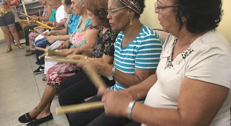 O Grupo Alegria, coordenado por um médico do Centro de Saúde Pompeia, se reúne todas as terças-feiras, às 8h da manhã. Foto: Divulgação PBH Sete idosas brincam de tocar baquetas.
