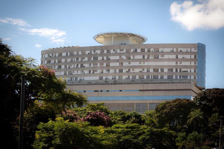 Hospital Célio de Castro renova título de entidade beneficente e economia com tributos é revertida ao atendimento Imagem aérea do hospital de frente. Em primeiro plano muitas árvores e em segundo plano um prédio branco, com detalhes e vidro e um heliporto na parte superior.