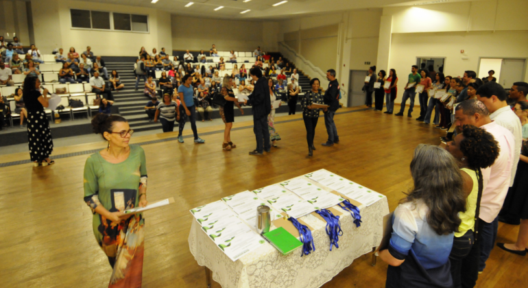 A PBH concedeu certificado a escolas da rede municipal por adotar ações de sustentabilidade ambiental como a economia do uso de água. Foto: Rodrigo Clemente/PBH auditório com mais de trinta pessoas, e uma fila com mais de vinte pessoas para receber os muitos certificados, dispostos em cima de uma mesa.