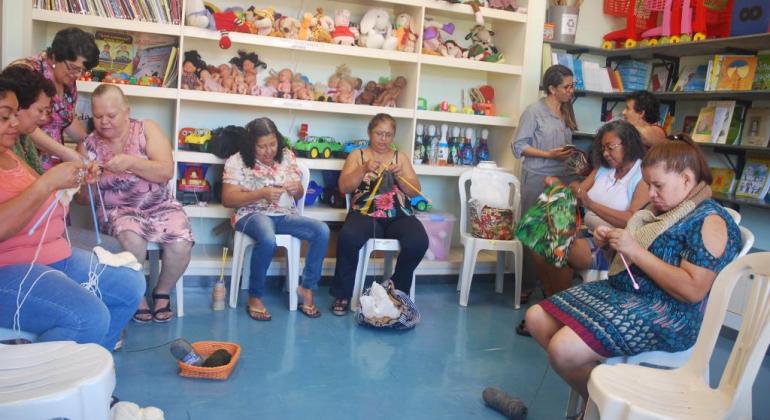 Na região Nordeste, projeto visa fortalecer os laços entre a escola e a comunidade e estimular o aprendizado e o convívio social. Foto: Mara Damasceno/PBH Sete mulheres tricotam em biblioteca.