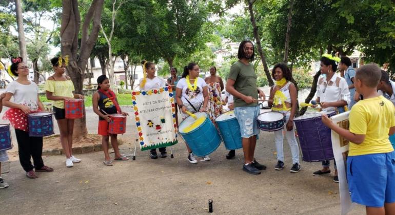 Se foliões de diversas idades, a maioria com instrumentos de percussão nas mãos, duas delas com estandarte. Um dod estandartes tem os dizeres: "Arte na saúde: Ateliê de Cidadania Regional Nordeste". 