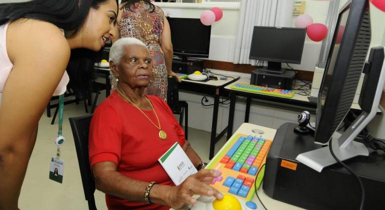 Senhora idosa faz curso de informática acompanhada por monitora da Prodabel. 