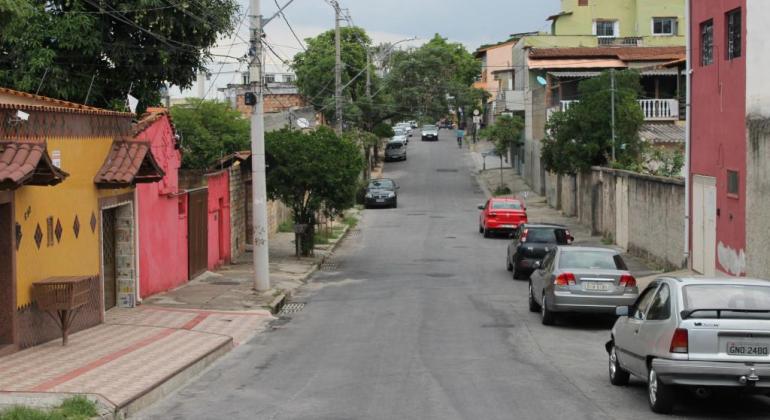 Foto de rua pavimentada com quatro carros estacionados, durante o dia. 