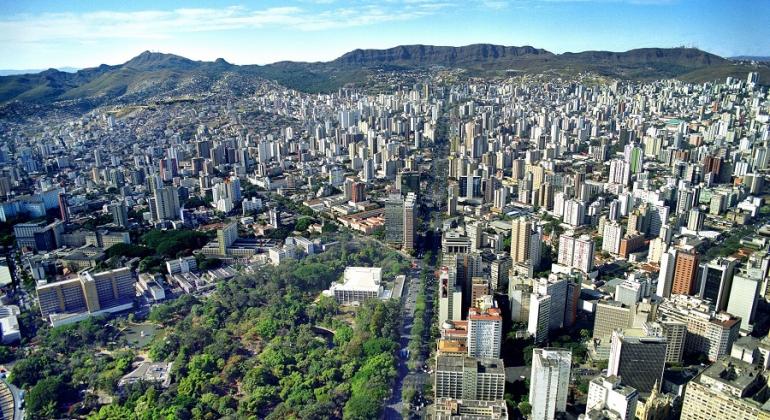 Vista aérea da avenida Afonso Pena, com Parque Municipal à esquerda, abaixo, prédios por todos os lados e a Serra do Curral ao fundo. 