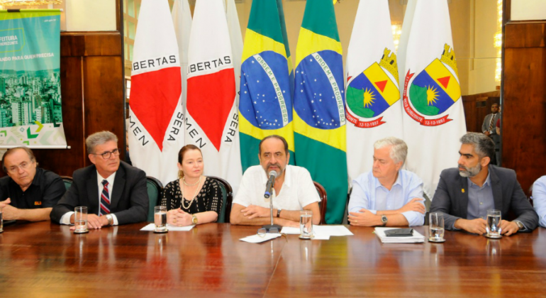 Prefeito assina contratos de financiamento de R$ 160 milhões para investimento em prevenção de enchentes e gestão de resíduos. Foto: Amira Hissa/PBH Prefeito e secretariado assinam convênio com representantes da Caixa Econômica Federal, todos sentados na mesa do Salão Nobre da PBH.