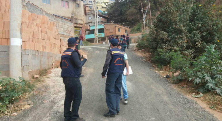 Um dos exercícios simulados será o fechamento da via em vários pontos, com a colocação de barreiras para evitar o tráfego de veículos. Foto: Divulgação PBH Dois técnicos da Defesa Civil acompanham cidadão em vila, mais à frente, outros dois técnicos caminham. Foto ilustrativa.