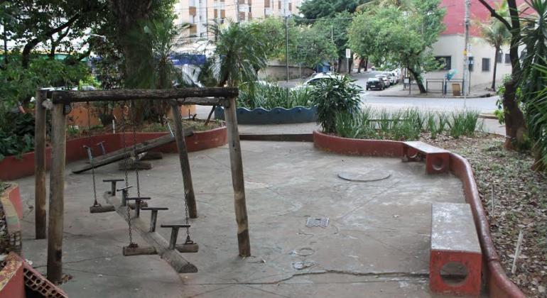 Praça Leonardo Gutierrez, com brinquedo infantil e vanco e praça, além de árvores e outras plantas, durante o dia. 