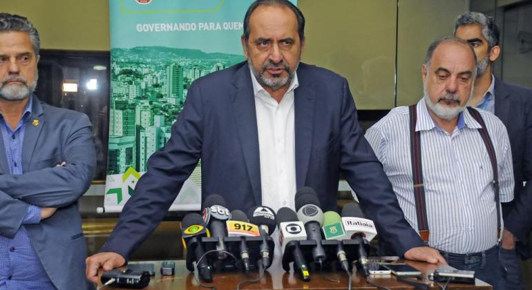 Prefeito decreta emergência em áreas afetadas pelas chuvas e estabelece prazo para realização de obras para evitar inundações em Venda Nova. Foto: Amira Hissa/PBH Superintendente da Sudecap, Henrique Castilho, prefeito de Belo Horizonte, Alexandre Kalil, secretário municipal da Fazenda, Fuad Noman, à frente de mesa para entrevista com microfone de várias rádios e emissoras de TV.