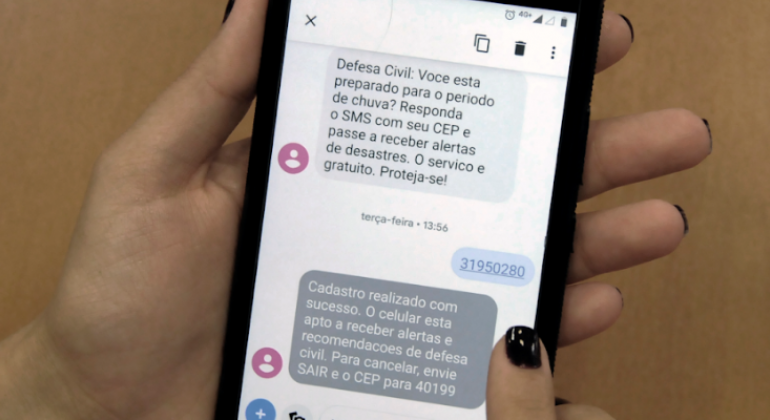 A Prefeitura firmou uma parceria com a CBTU, empresa que administra o metrô, para divulgação de alertas preventivos de chuvas fortes. Foto: Divulgação PBH Mão feminina segura celular com alertas de chuva por meio de mensagem.