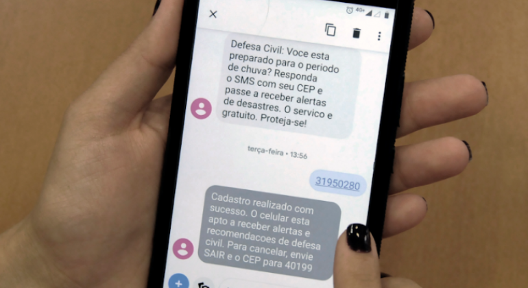 Mão feminina segura celular com alertas de chuva por meio de mensagem. 