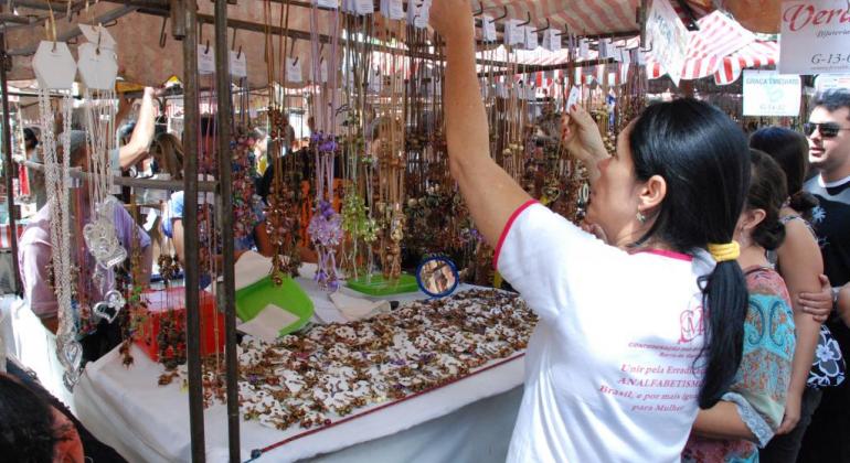 Imagem de uma mulher observando algumas peças de artesanato em uma feira