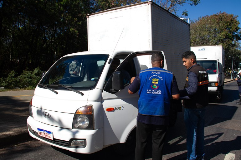 Blitz da Operação Oxigênio identifica possíveis irregularidades em nove veículos Dois fiscais da Prefeitura de Belo Horizonte vestido coletes da PBH um deles na cor azul e outro na preta, abordam motorista de um caminhão de porte pequeno na cor branca