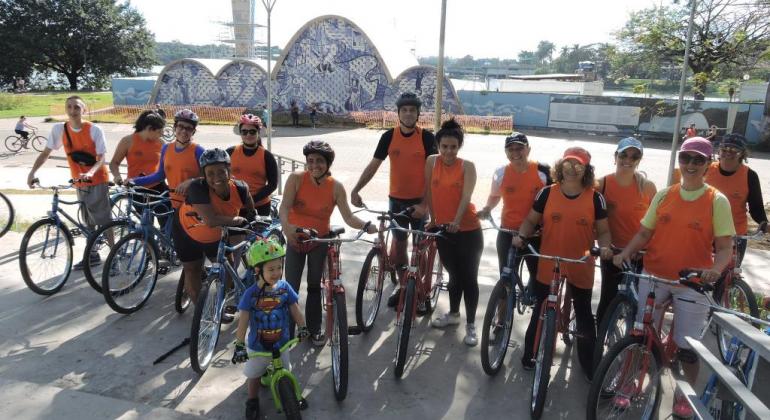Foto: Andréa Moreira/PBH Doze alunos e uma criança, cada um com sua bicicleta, na frente da Igrejinha da Pampulha, durante o dia.