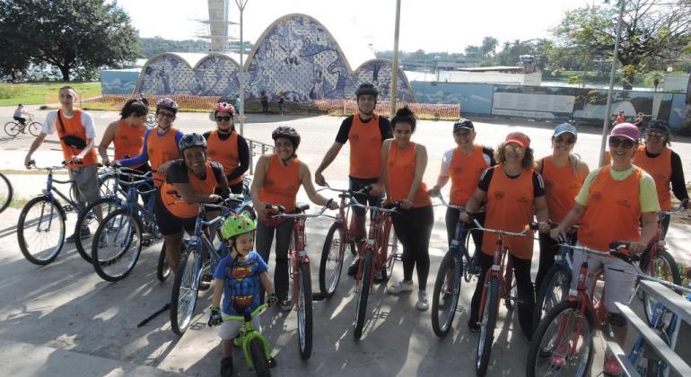 Doze alunos e uma criança, cada um com sua bicicleta, na frente da Igrejinha da Pampulha, durante o dia. 