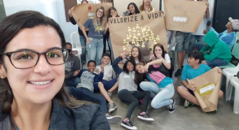 Selfie de mulher com mais de doze jovens com cartazes sobre o combate à automutilação. 