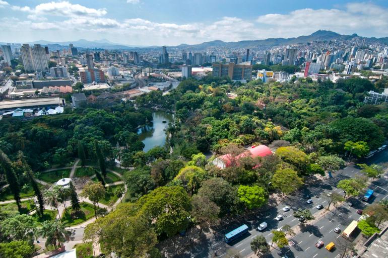 Vista aérea do Parque Municipal. No entorno, avenida e automóveis e ao fundo, edifícios e o contorno de montanhas.