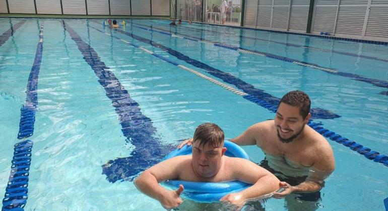 Aluno com necessidades especiais aproveita a piscina ao lado de um monitor do Centro de Referência Esportiva para a Pessoa com Deficiênci