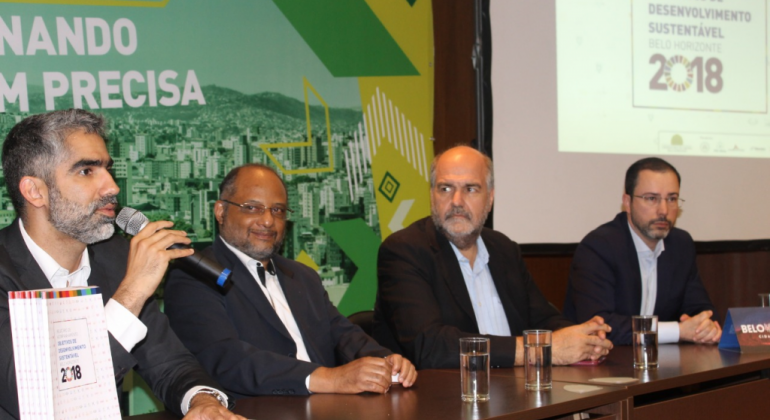 Belo Horizonte lança relatório dos Objetivos de Desenvolvimento Sustentável Quatro homens sentados. Um deles é o secretário municipal de planejamento, André Reis, que fala ao microfone