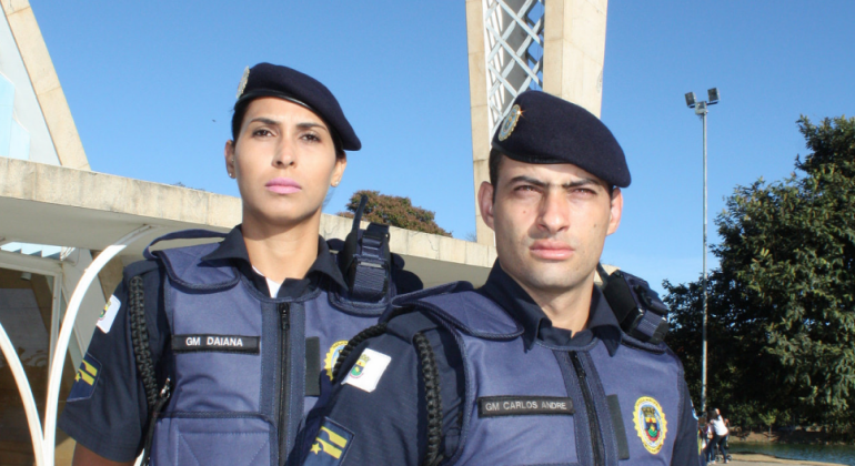 Guarda municipal mulher e guarda municipal homem, lado a lado, em frente a igrejinha da pampulha