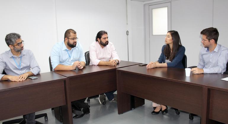 Três membros da Prefeitura conversam com duas pessoas de segmentos, em uma sala. 