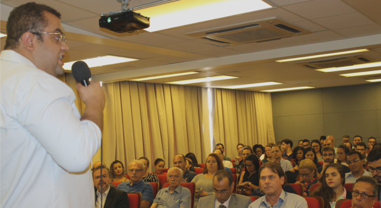 Homem palestra para mais de cinquenta profissionais da área contábil, em auditório. 