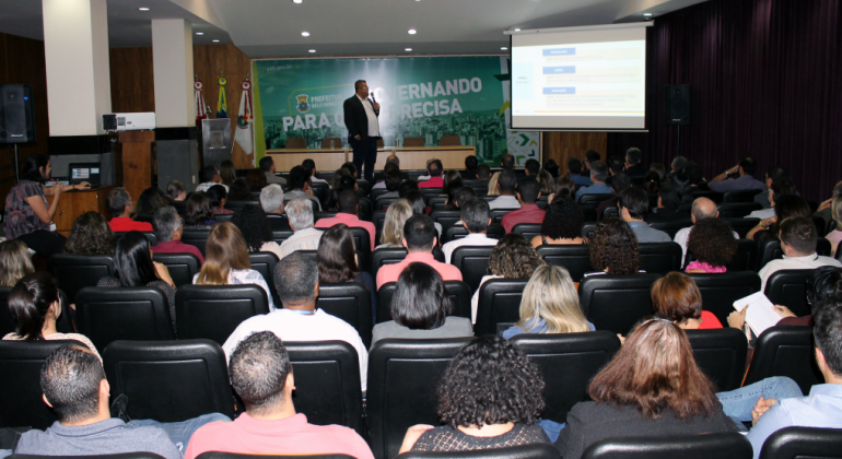 Corpo gerencial da Prefeitura é apresentado a solução que modernizará os processos das áreas financeira e administrativa. Foto: Divulgação PBH Homem, de pé, palestra para mais de cinquenta pessoas sentadas no salão JK, da Prefeitura.