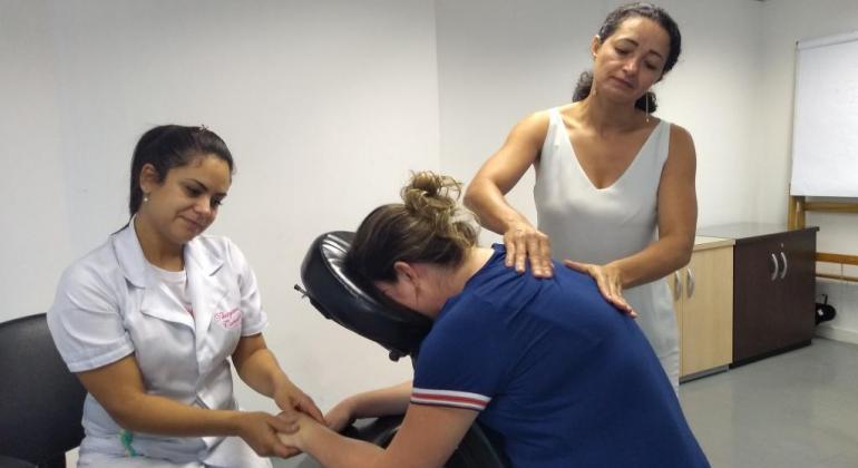 A Quick Massage tem duração de 15 minutos e utiliza manobras adaptadas das técnicas orientais para proporcionar o relaxamento muscular. Foto: Divulgação PBH Mulher sentada com apoio no rosto recebe massagem de duas técnicas.