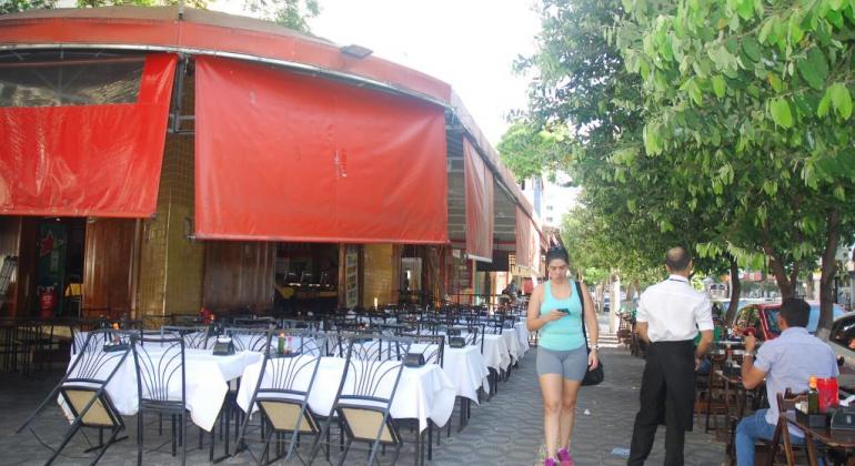 Cidadã caminhando tranquilamente em calçada ao lado de restaurante