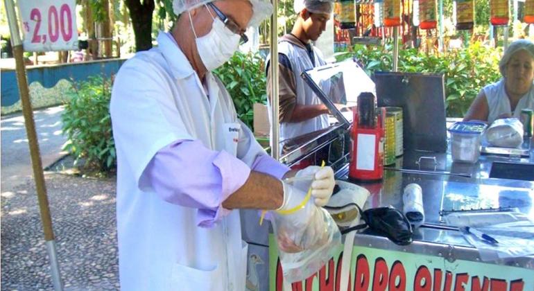 Vendedor de cachorro-quente, com touca e luvas, durante o dia. 