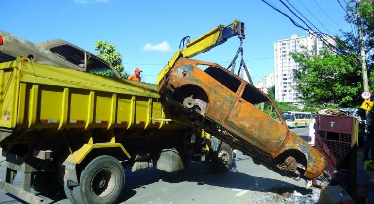 Caminhão reboca carro abandonado durante o dia. 