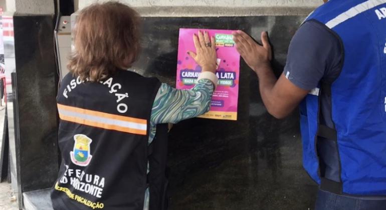 “Carnaval é na lata” combate a venda de bebidas em garrafas de vidro Equipe da Subsecretaria de Fiscalização colando o cartaz do “Carnaval é na lata”
