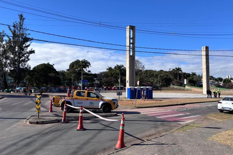 Operações de trânsito para eventos nas regionais Centro-Sul, Noroeste e Barreiro, neste final de semana Fotografia em dia ensolarado da Praça da Pampulha, com uma caminhonete amarela da BHTRANS estacionada em uma ilha de trânsito isolada por cones e fita zebrada.