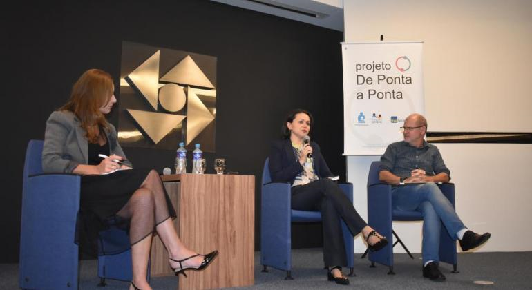 Em Novo Hamburgo-RS, Prefeitura apresenta experiência da implementação do Marco Regulatório em Belo Horizonte. Foto: Fundação Semear Duas mulheres e um homem fazem exposição, sentados, em Hamburgo.