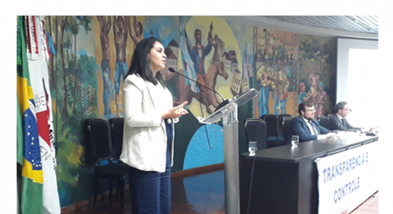 PGM apresenta experiência de implementação da Lei 13.019/2014 Mulher fala ao microfone e apresentação de palestra