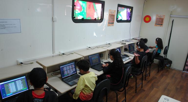 Cinco crianças, sentadas dentro da van do projeto Conexão Aberta, aprendendo a navegar na internet e lidar com os computadores dispostos no painel à frente. Foto ilustrativa, de edições anteriores do projeto. 