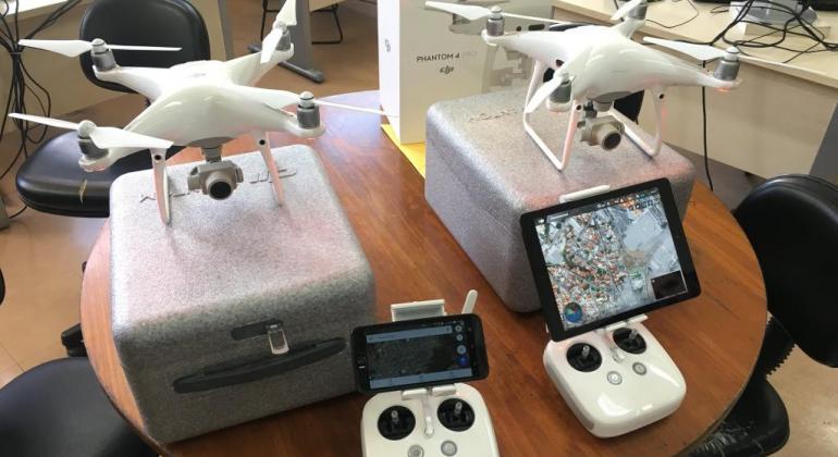 Dois drones com seus respectivos controles em cima de uma mesa. 