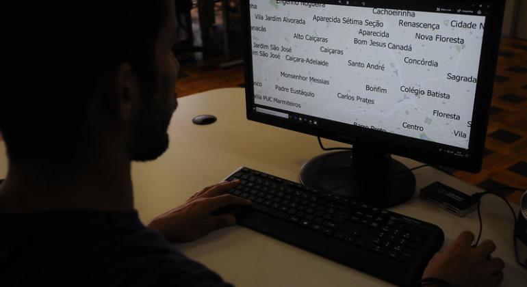 A capital mineira tem 331 km² e conta com 15.992 logradouros (ruas, becos, estradas, túneis, avenidas etc.) em 487 bairros. Foto: Rodrigo Clemente/PBH Homem em frente ao computador com mapa de Belo Horizonte, com os nomes de bairros, na tela.