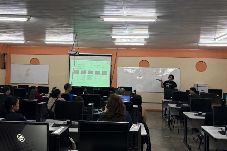 Curso gratuito de informática básica da PBH ensina a usar ferramentas do Google e acessar serviços digitais Sala de aula, com computadores nas mesas, alunos presentes e professor em frente ao quadro branco.
