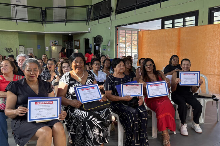 Idosos descobrem poder da Inteligência Artificial na Regional Norte Uma sala cheia de idosos, na maioria mulheres, brancas, pardas e pretas, seguram o certificado de conclusão do curso.