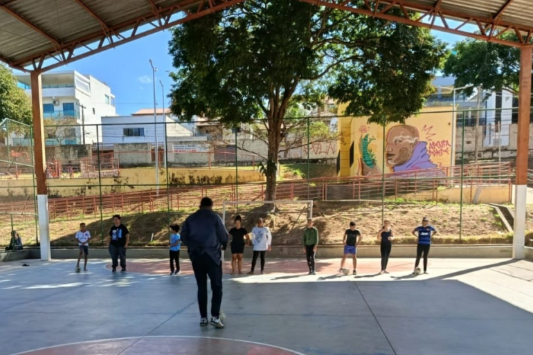 Projeto Providência em Ação abre inscrições para a nova escolinha de futsal meninos em uma quadra de futebol coberta, todos em uma linha horizontal de frente para um adulto, que está de costas para a foto.