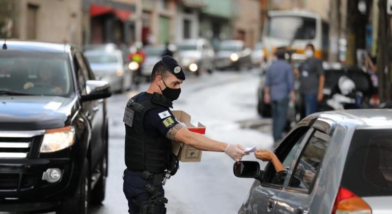 Prefeitura faz entrega de máscaras para população de aglomerados Agente da Guarda Civil Municipal distribuindo máscara para população que vive em aglomerados da capital